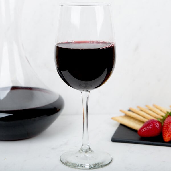 A Libbey Vina tall wine glass filled with red wine next to strawberries on a table.