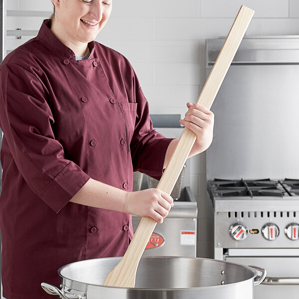 A woman in a chef's uniform stirring a pot with a Choice 42" wood paddle.