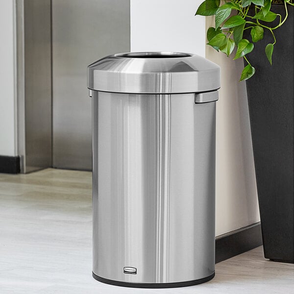 A Rubbermaid stainless steel round waste container next to a plant.