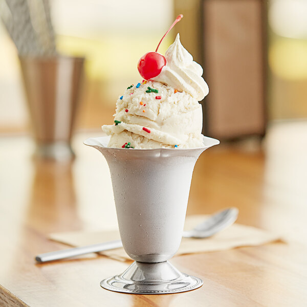 A white stainless steel tulip dessert dish filled with ice cream and a cherry on top.