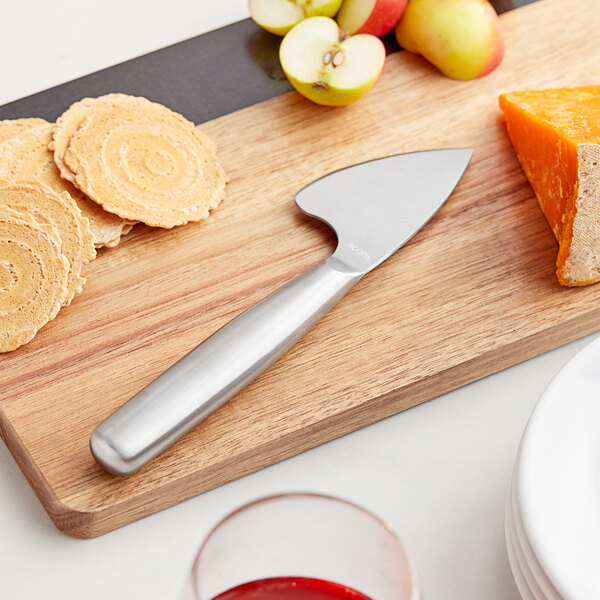 An Acopa hard cheese cleaver on a cutting board with cheese, fruit, and crackers.
