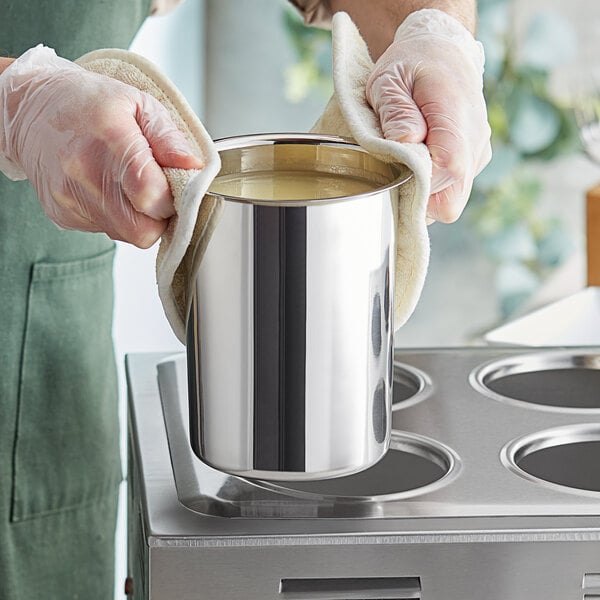 A person in gloves holding a stainless steel Bain Marie pot of liquid.
