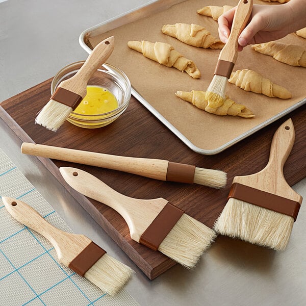 A person using a Boar Bristle pastry brush to paint croissants on a tray.