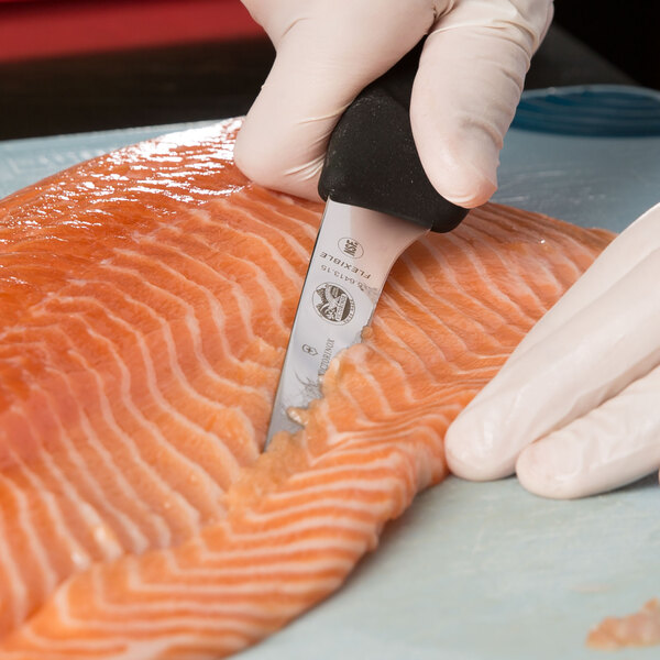 A person in gloves using a Victorinox curved boning knife to cut a piece of fish.