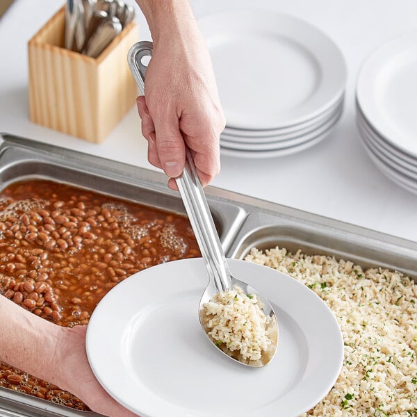 A person using a Choice stainless steel basting spoon to serve food on a plate.