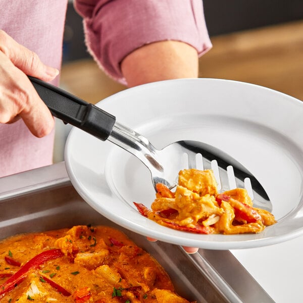 A person using a Choice 11" slotted stainless steel basting spoon to serve food from a bowl.