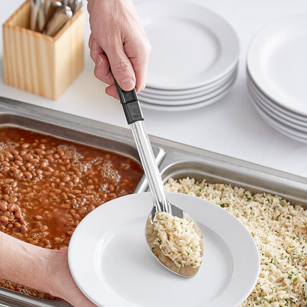 A person using a Choice solid stainless steel basting spoon with a coated handle to serve rice and beans.