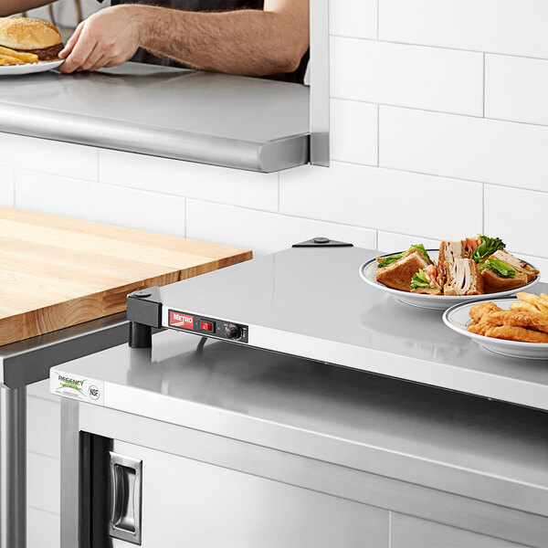 A man using a Metro Stainless Steel Countertop Shelf Warmer to keep plates of fried food warm.