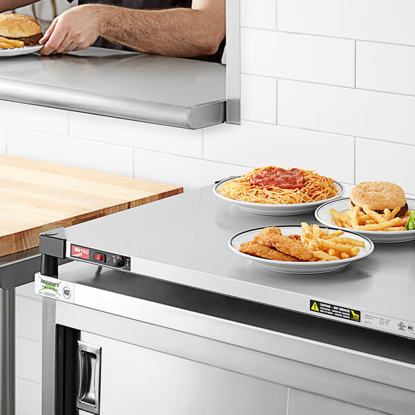 A man using a Metro stainless steel countertop shelf warmer to keep a plate of burgers and fries warm on a counter.