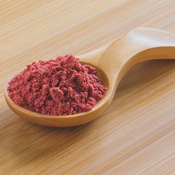 A wooden spoon full of red Organic Strawberry Powder.