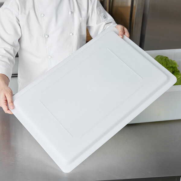 A chef holding a white rectangular Rubbermaid lid.