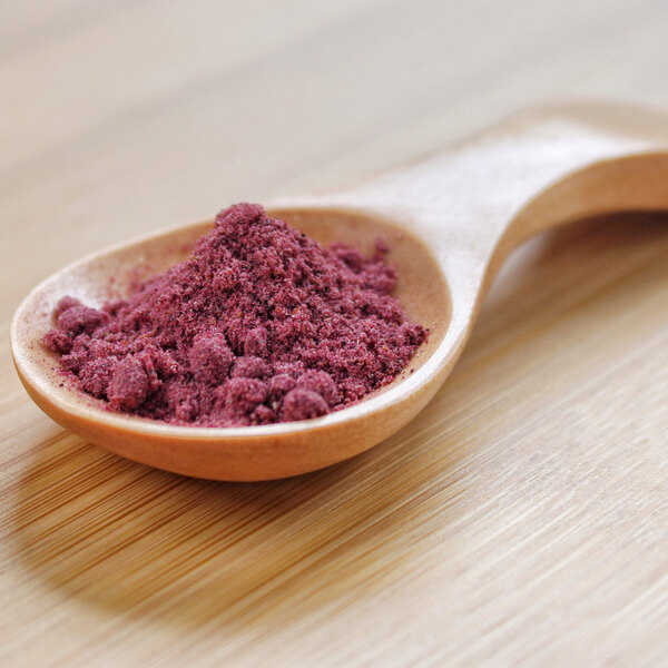 A wooden spoon filled with blueberry powder.
