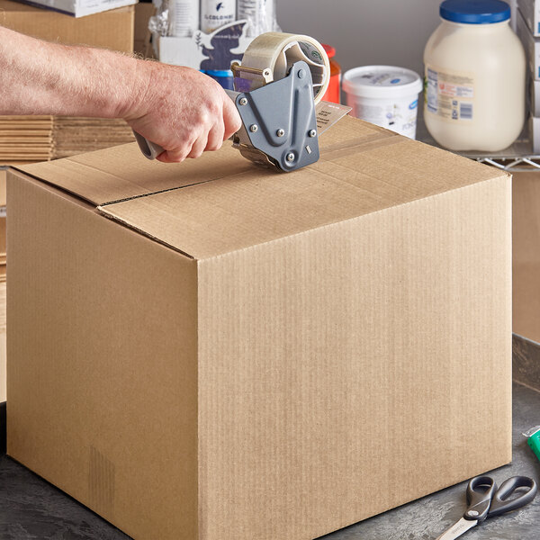 A hand cutting open a Lavex Kraft corrugated shipping box with a box cutter.