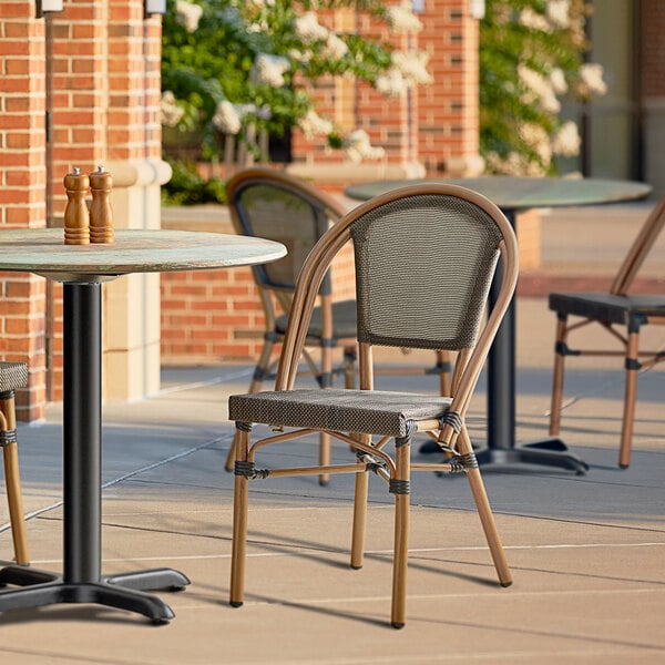 A Lancaster Table & Seating French Bistro Brown Outdoor Side Chair on a patio with a table.