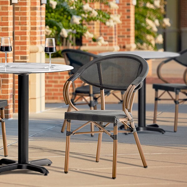 A Lancaster Table & Seating French Bistro Black Outdoor Arm Chair on a patio.