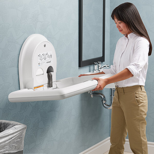 A woman holding a Koala Kare white granite baby changing station.