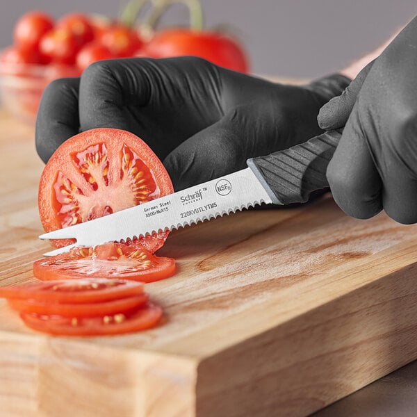 A person in black gloves using a Schraf serrated tomato knife to cut a tomato.