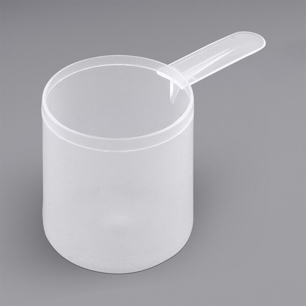 A clear plastic container with a white circle and a clear plastic scoop with a short handle.