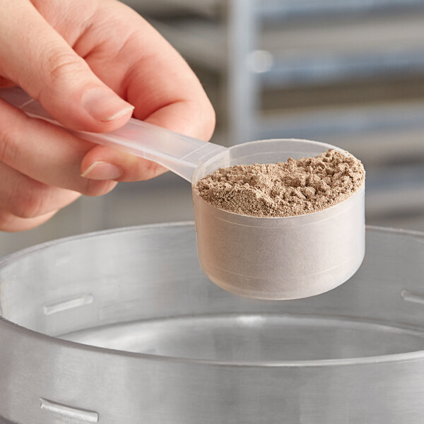 A person using a long-handled polypropylene scoop to measure brown powder from a metal container.