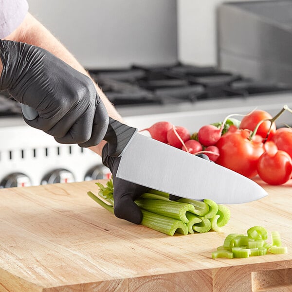 A person in black gloves using a Schraf chef knife to cut celery on a cutting board.