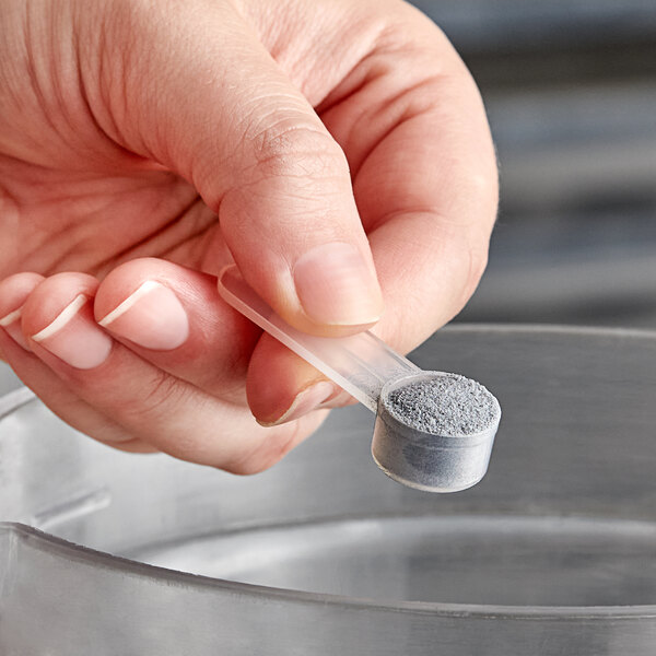 A person using a 1.25 cc polypropylene scoop to measure grey powder.