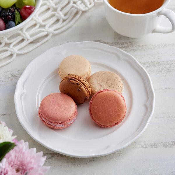 A white Acopa Condesa scalloped porcelain plate with a pink macaron, cookies, and a cup of tea.