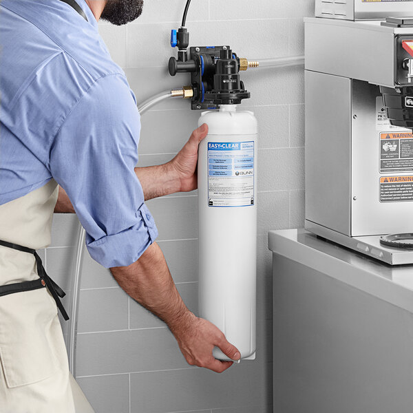 A man holding a Bunn water filtration cartridge in a professional kitchen.