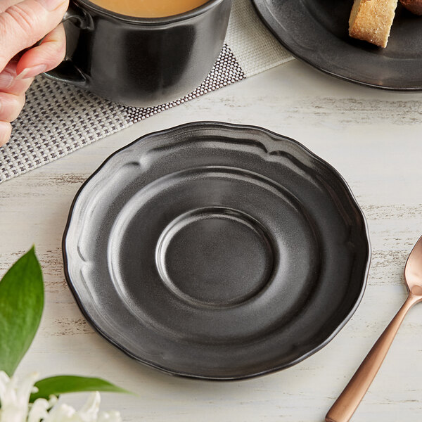 A hand holding an Acopa Condesa matte gray porcelain saucer with a mug of coffee next to a plate with food.