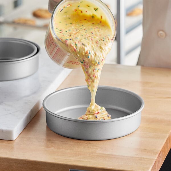 A person pouring cake batter into a Baker's Mark round cake pan.