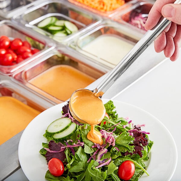 A person using a Choice stainless steel ladle to pour dressing over a salad.