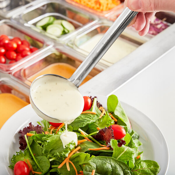 A person using a Choice stainless steel ladle to pour white dressing over a salad.
