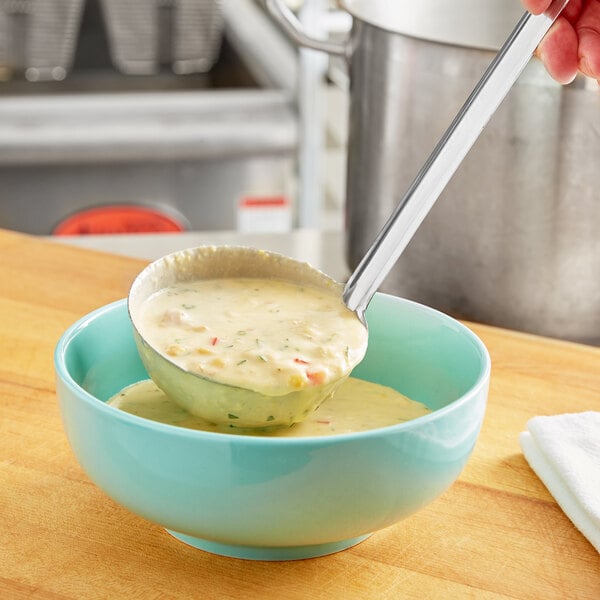 A person holding a Choice stainless steel ladle over a bowl of soup.