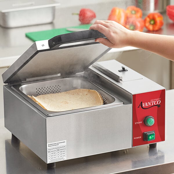 A person using an Avantco stainless steel countertop tortilla steamer to steam a tortilla.