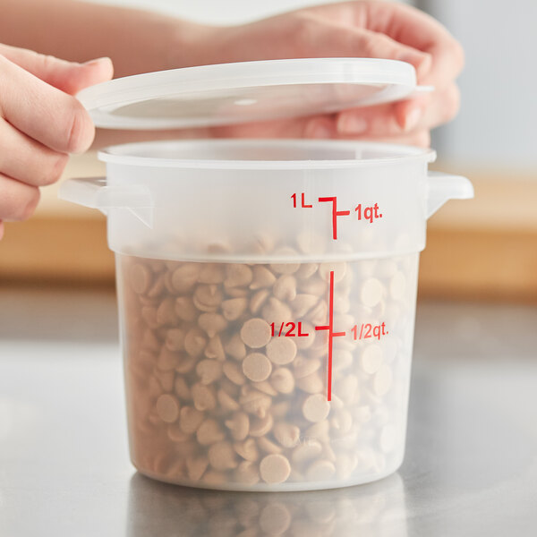 A person holding a Choice translucent round plastic food storage container filled with small brown dots with the lid open.