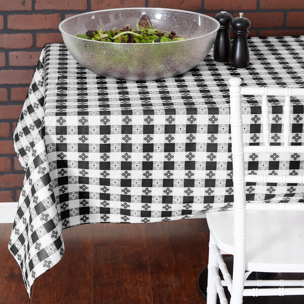 A white table with a black and white checkered vinyl table cover and a bowl of salad.