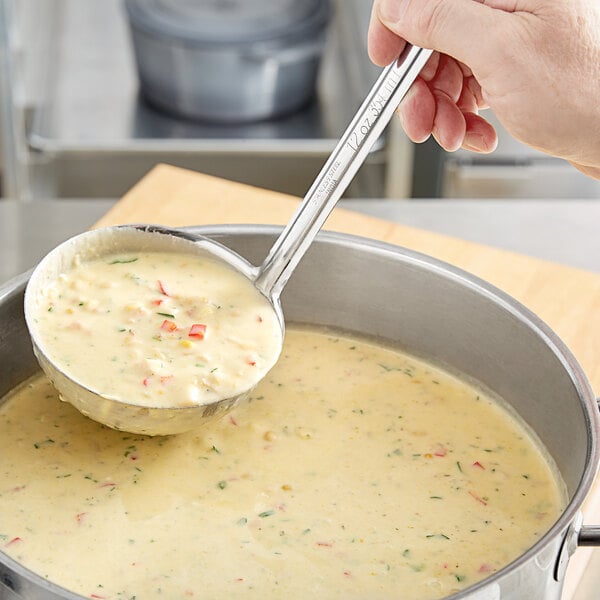 A person using a Choice stainless steel ladle to serve soup.