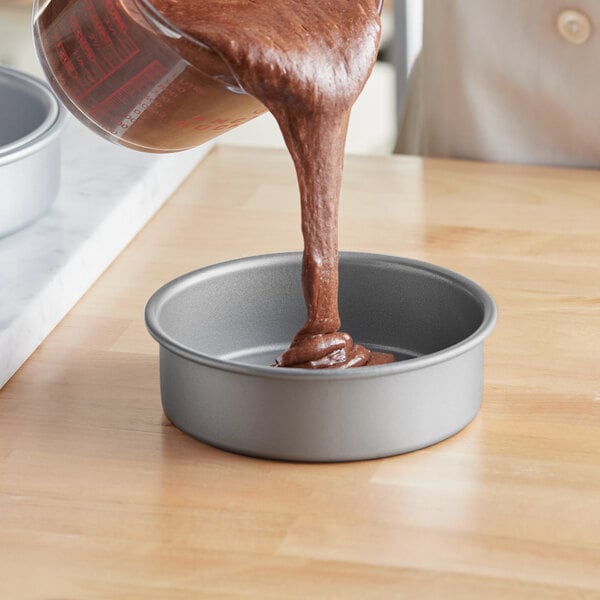 A person pouring brown liquid into a Baker's Mark round cake pan.