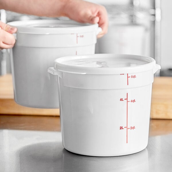 A person holding a measuring cup and a measuring bowl pours food into two white plastic Choice food containers.