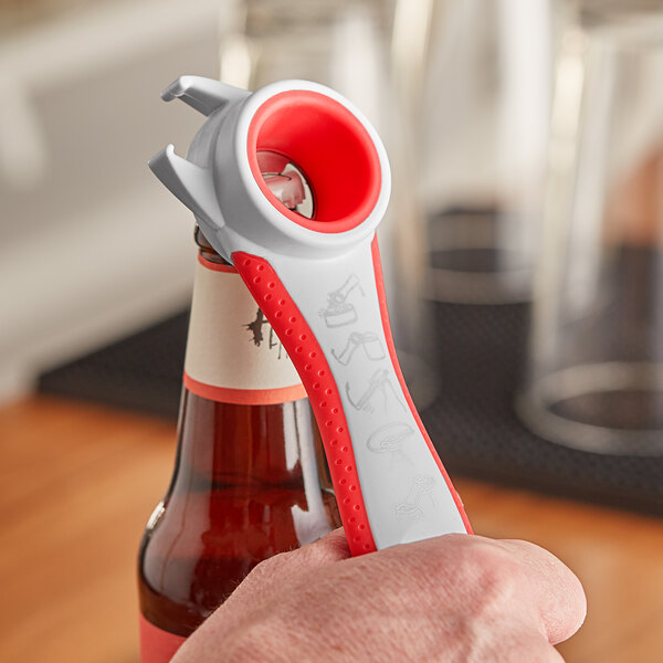 A person using a Franmara red multi-purpose bottle opener to open a bottle of beer.