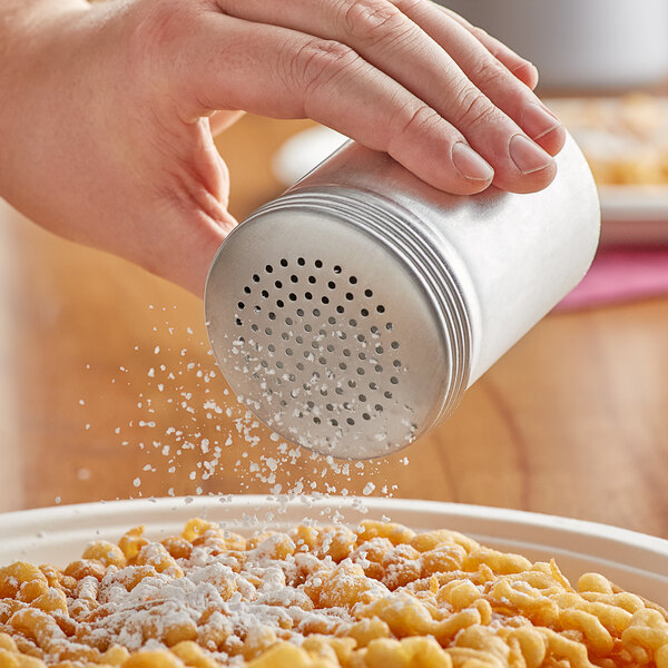 A hand holding a Choice aluminum shaker with powder being poured onto food.