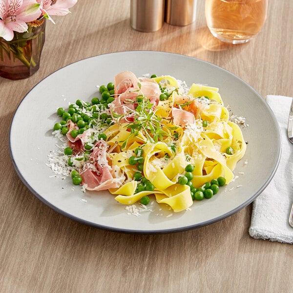 An Acopa matte grey and black melamine plate with pasta, ham, and peas.