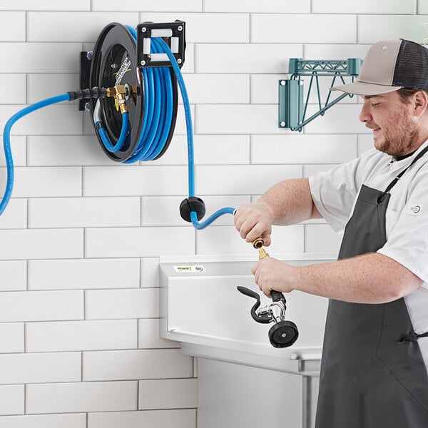 A man in a white shirt and apron using a Regency hose reel with a hose and spray valve.