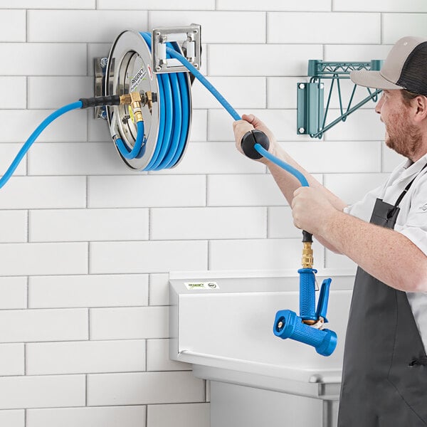 A man using a Regency stainless steel hose reel with a blue handle to connect a hose to a sink.