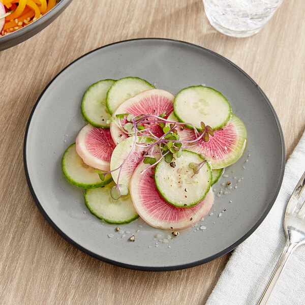 An Acopa Apollo matte grey and black melamine plate with sliced cucumbers and radishes on it.
