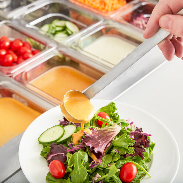 A person using a Choice stainless steel ladle to pour sauce over a plate of salad.