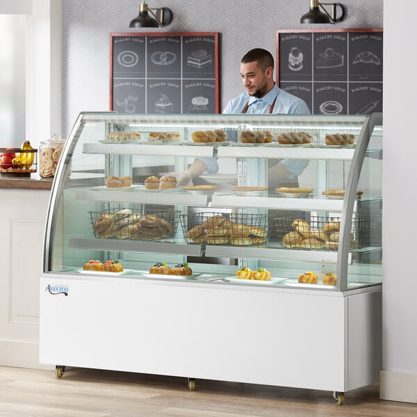 An Avantco white curved glass dry bakery display case on a counter with pastries displayed in it.