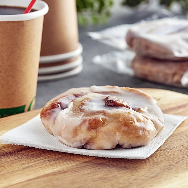 An individually wrapped Katz Gluten-Free Cinnamon Roll on a napkin next to a cup of coffee.