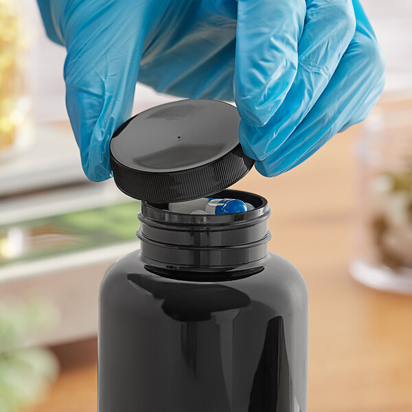 A gloved hand in blue gloves opening a black plastic bottle with a black ribbed cap.
