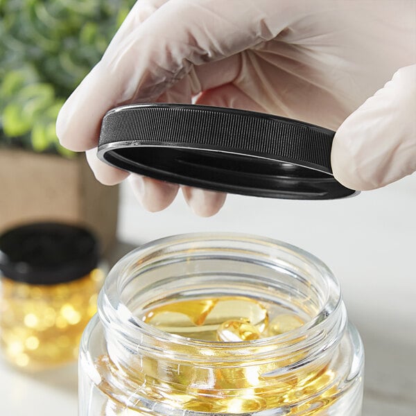 A hand holding a 70/400 black ribbed plastic cap over a jar of yellow liquid.
