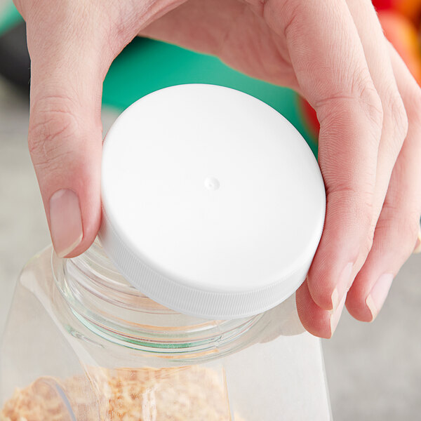 A hand holding a plastic container with a white 63/400 ribbed plastic cap on it.